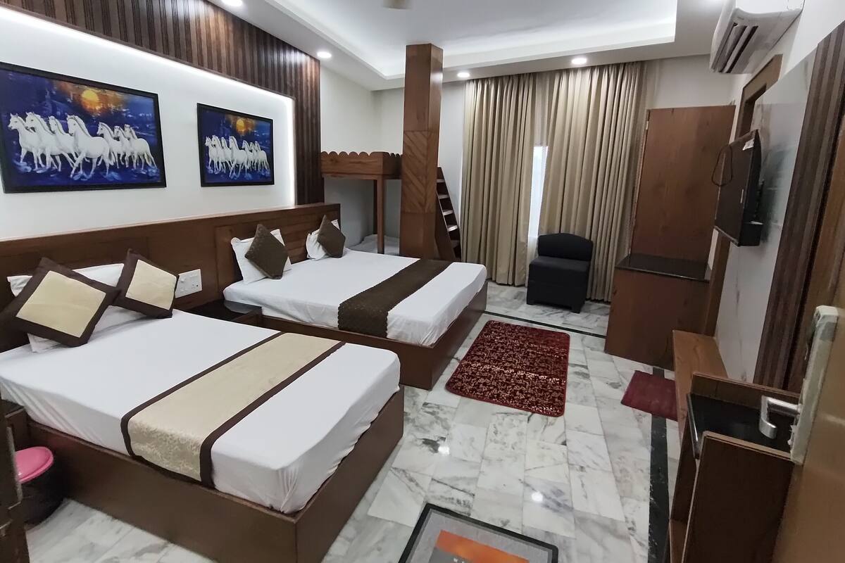 A hotel room with two beds, a TV, a ceiling fan, and a large window with curtains.