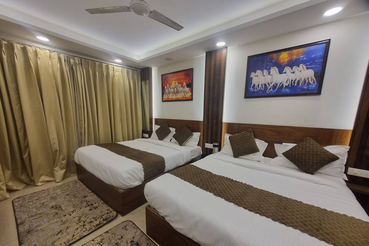 A hotel room with two beds, beige curtains, a ceiling fan, and two paintings on the walls.