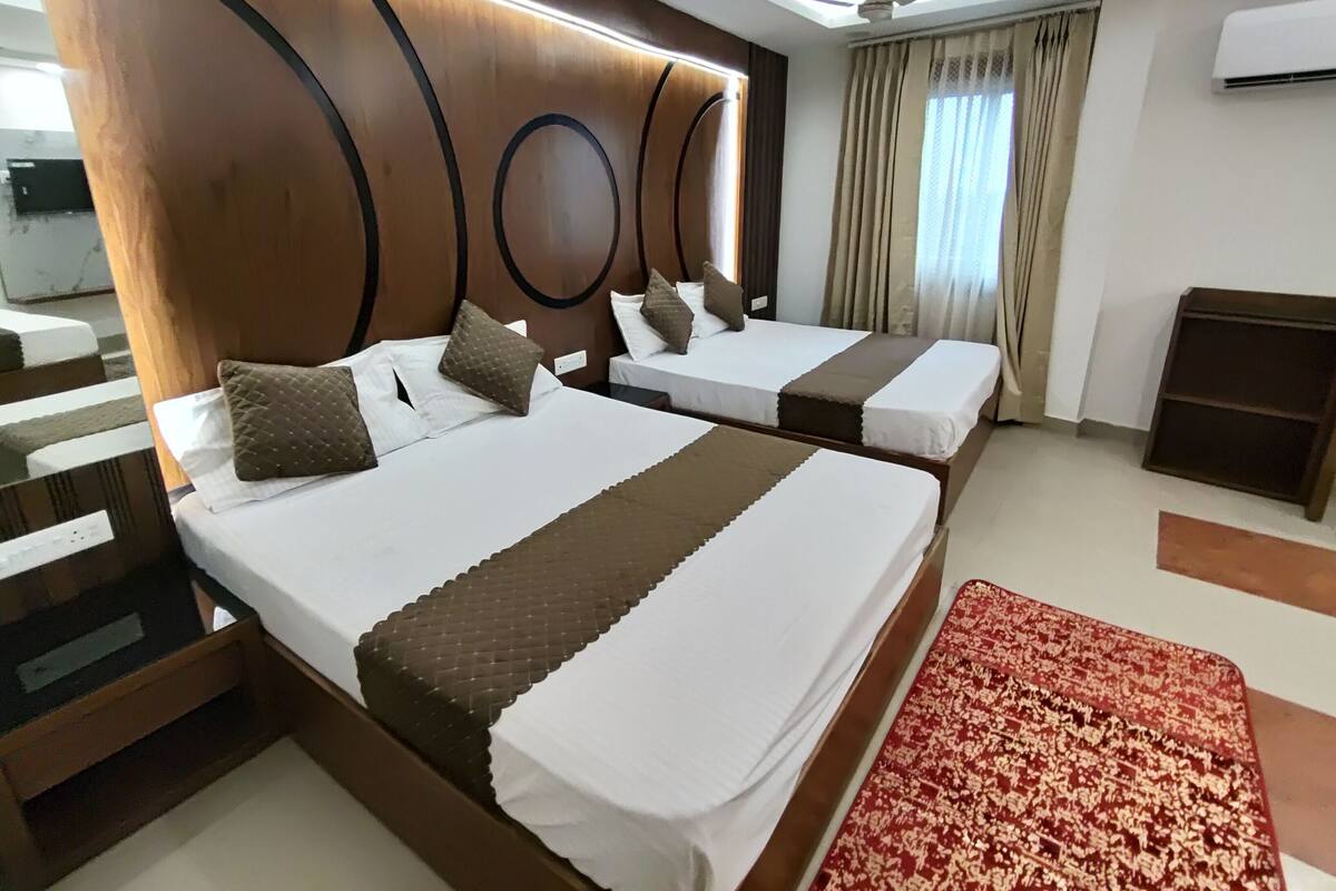 A hotel room with two beds, a ceiling fan, an air conditioner, and a red patterned rug.