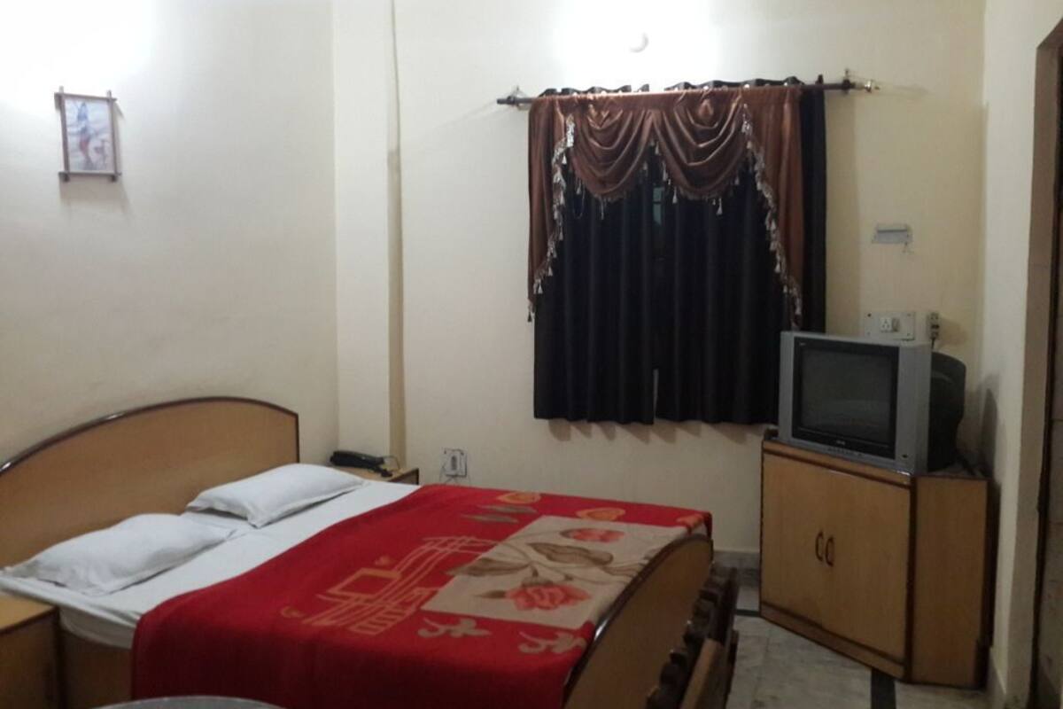 A bedroom with a bed, a television on a wooden cabinet, a window with curtains, and a small picture frame on the wall.