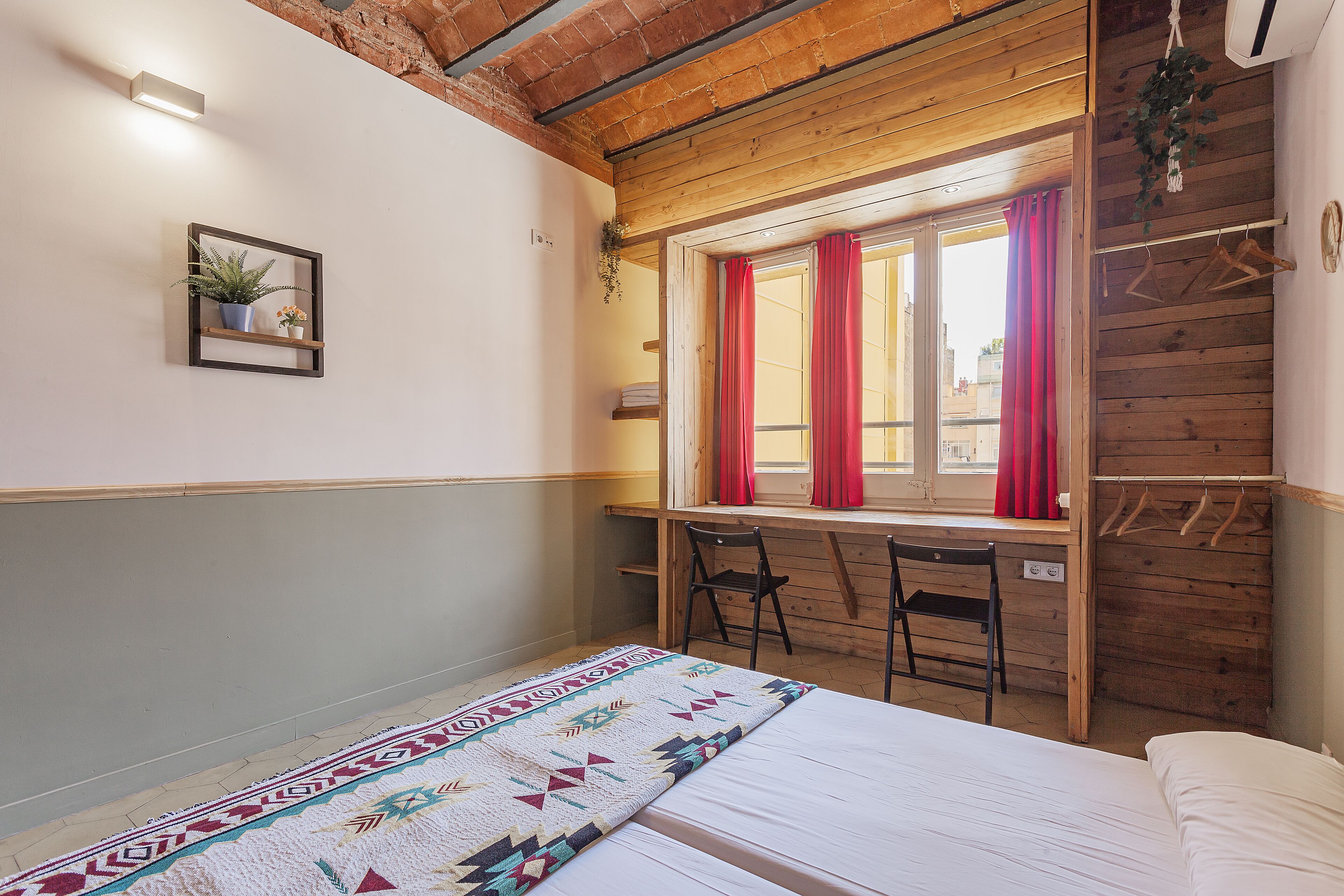 Una habitación con una cama, un escritorio con una silla, una ventana con cortinas y una planta colgante.