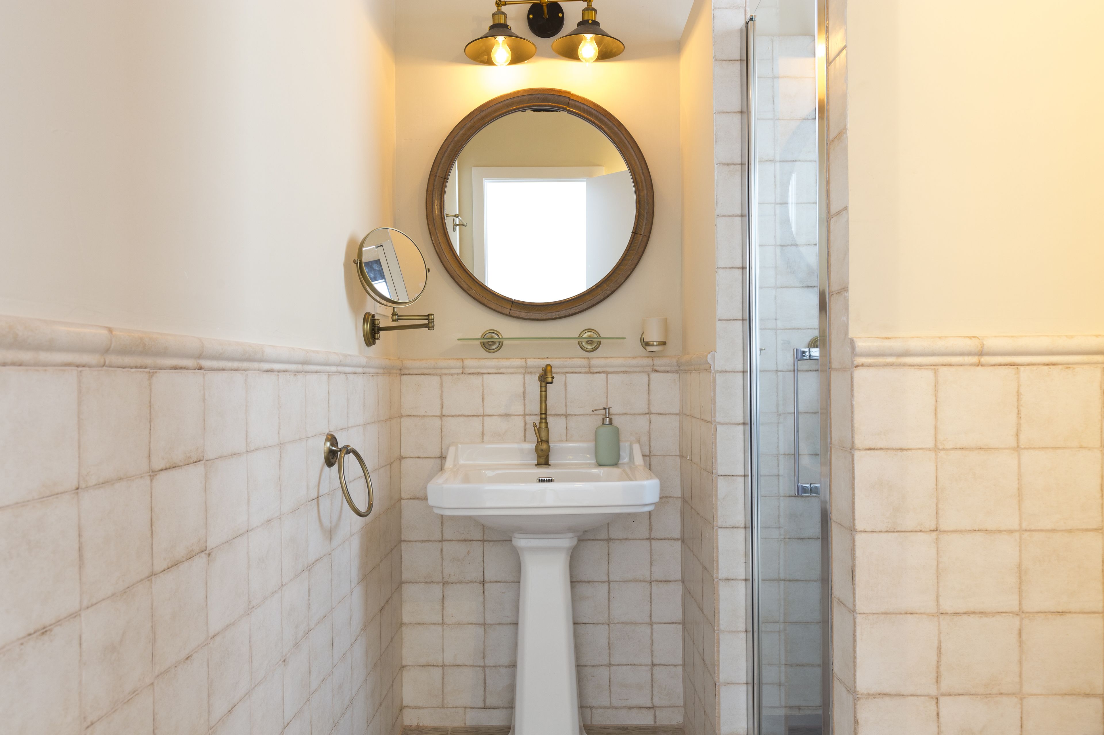 Un baño con lavamanos pedestal, un espejo redondo y cabina de ducha.