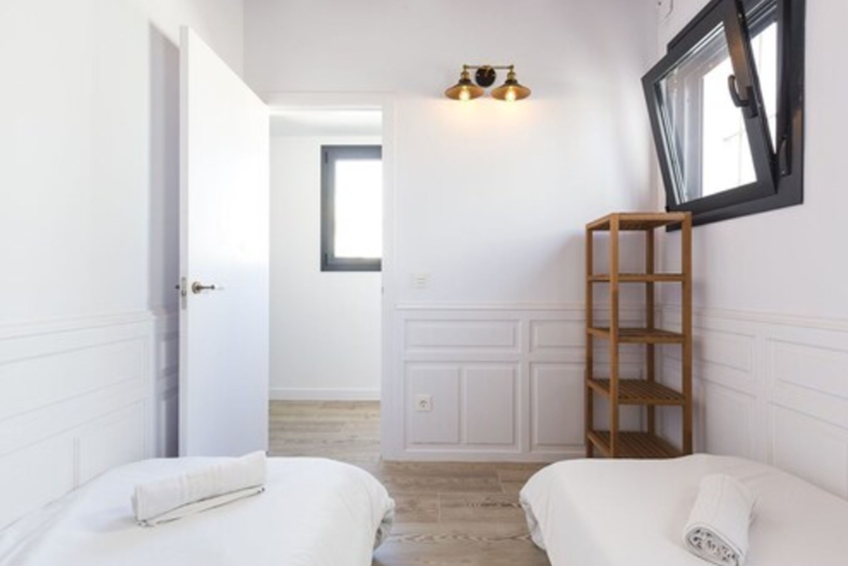 Slaapkamer met twee bedden, een houten plank, een wandlamp en een raam met zwarte lijst.
