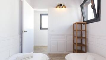 Slaapkamer met twee bedden, een houten plank, een wandlamp en een raam met zwarte lijst.