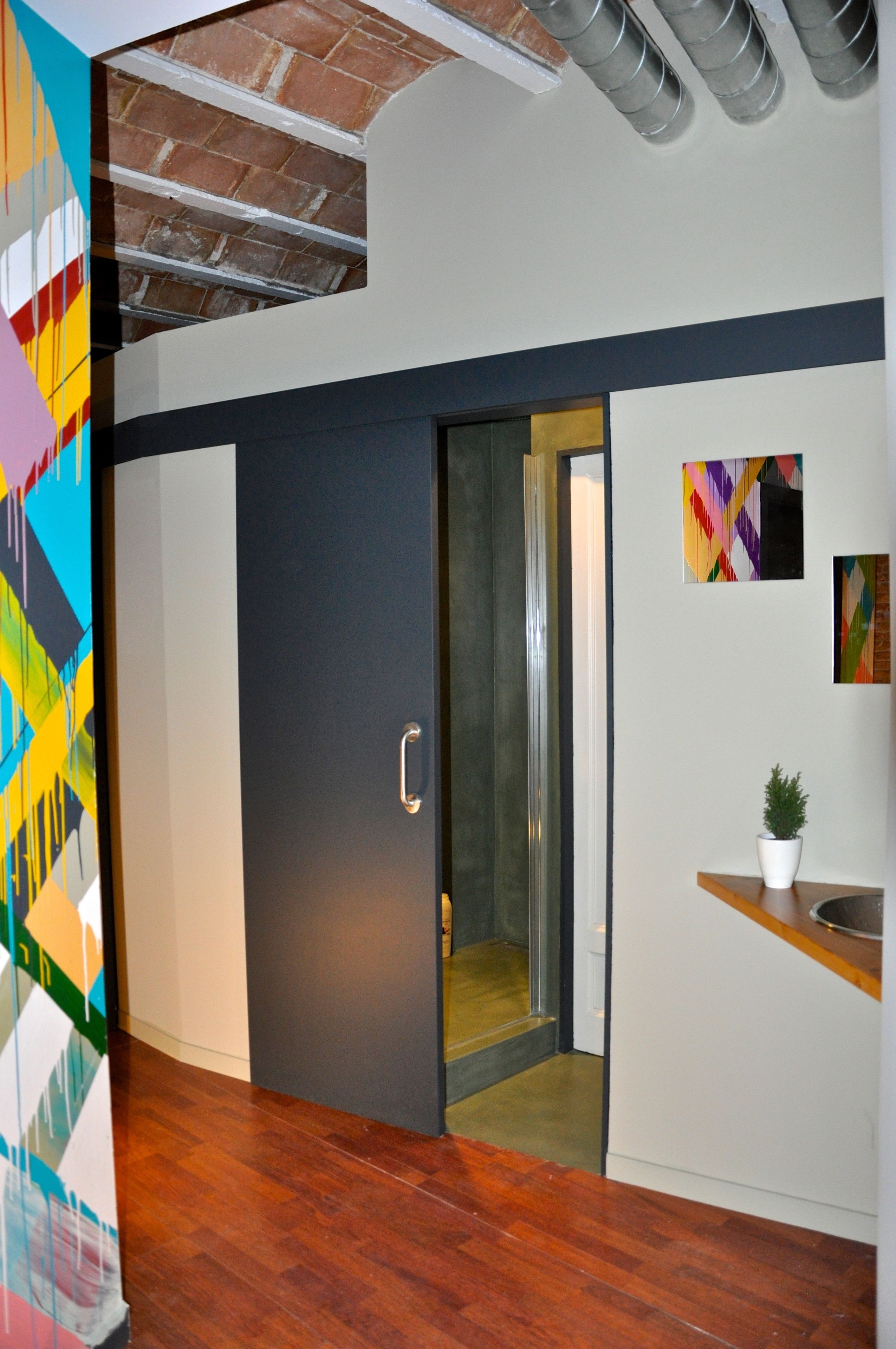 A modern interior with a wooden floor, a sliding door leading to a room, and a small potted plant on a counter.