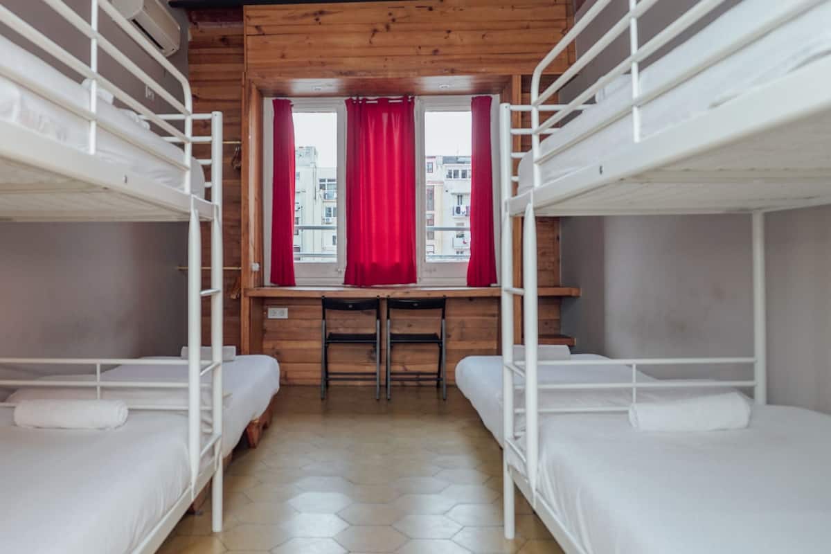 Um quarto de dormitório com beliches, uma escrivaninha de madeira e uma janela com cortinas vermelhas.