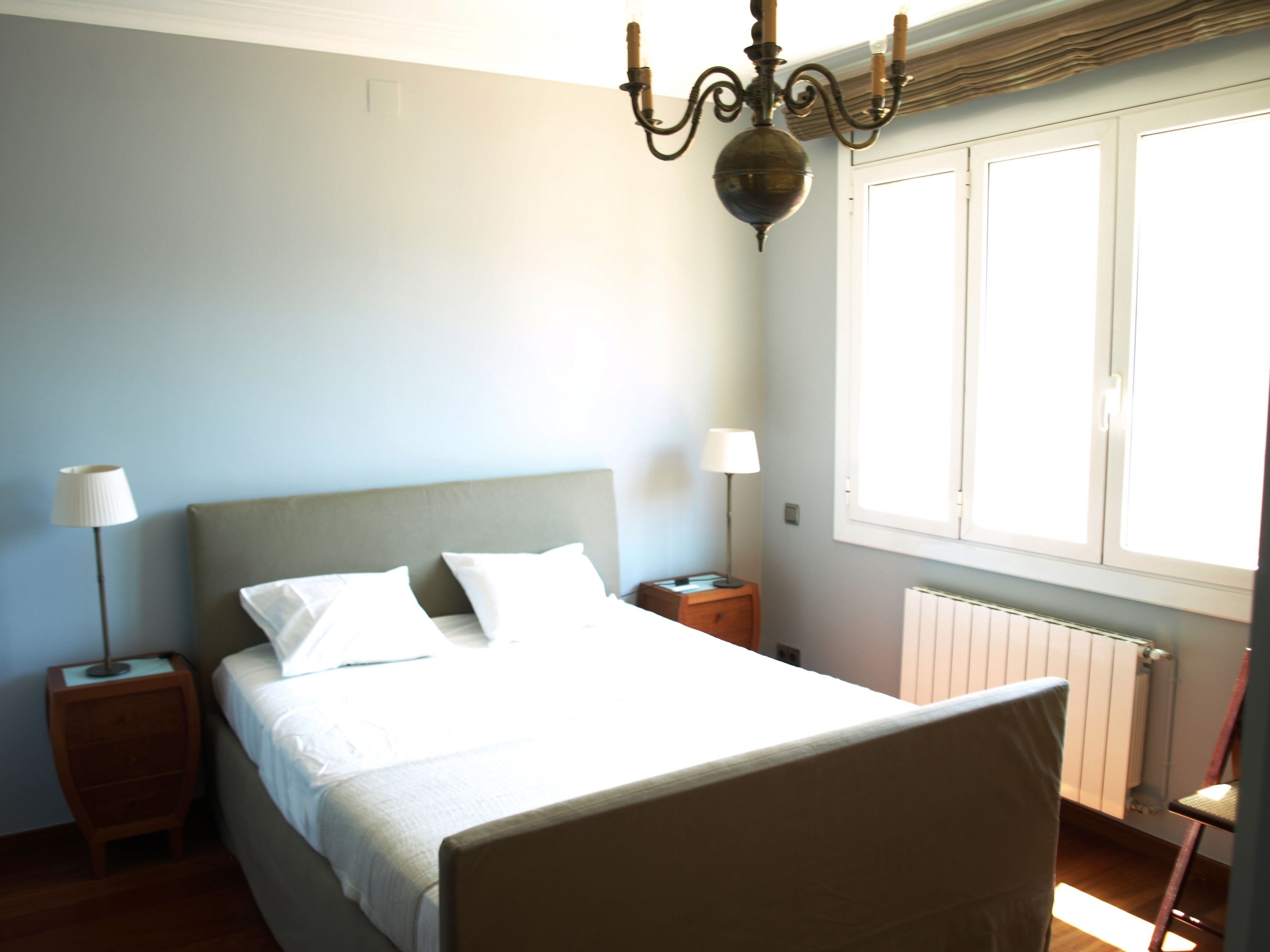 Un dormitorio con una cama, dos mesitas de noche, una lámpara, un radiador y una ventana.
