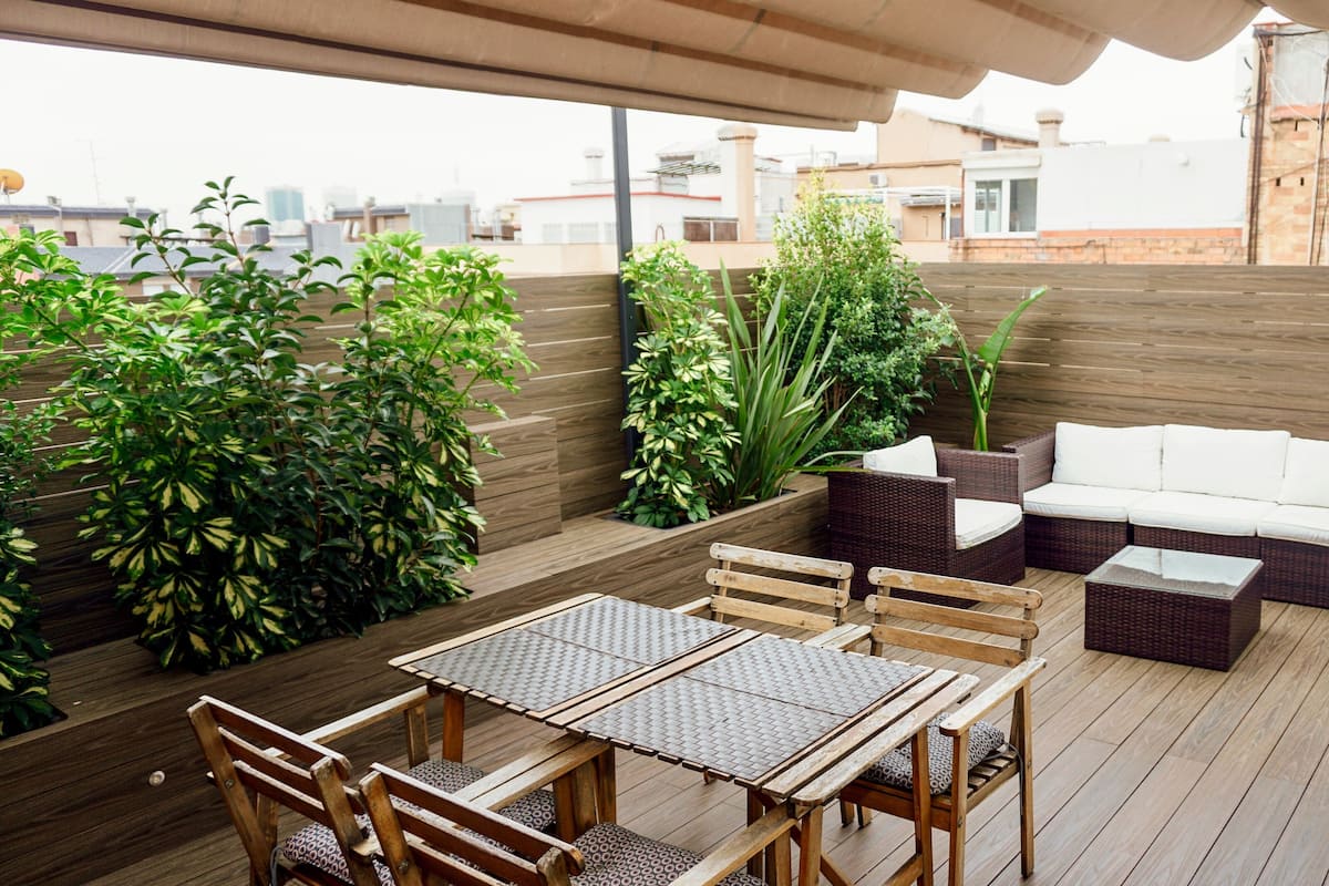 Um deck de madeira com mesa, cadeiras, um sofá e um abajur branco.