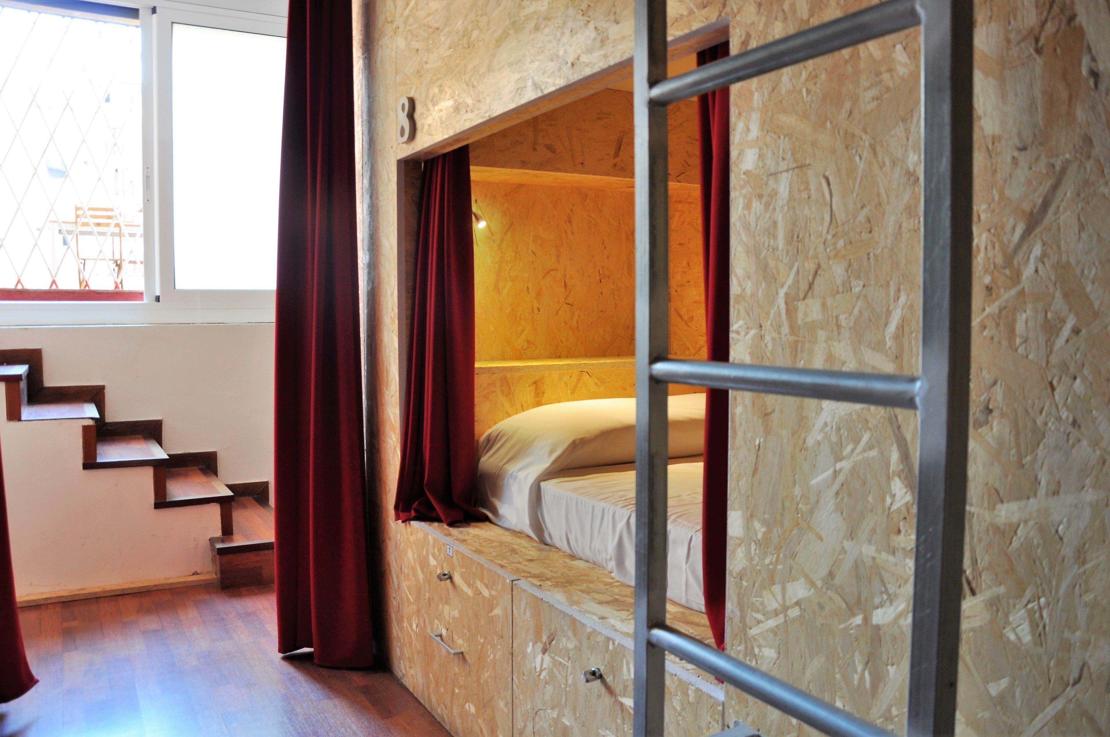 Habitación con literas, suelo de madera, una ventana con cortinas y una escalera.