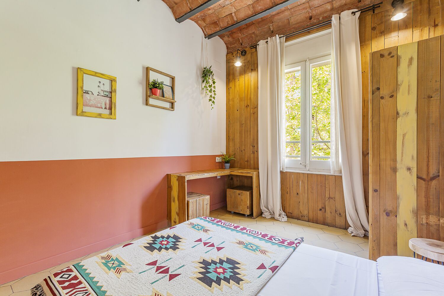 Una habitación acogedora con un escritorio de madera, una cama y un ventanal con cortinas.