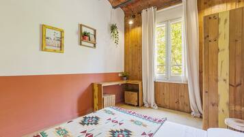 Una habitación acogedora con un escritorio de madera, una cama y un ventanal con cortinas.