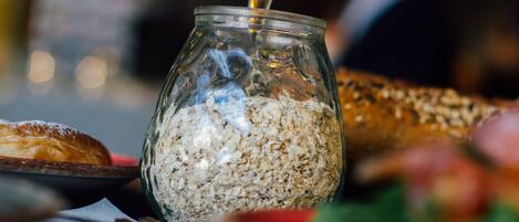 A glass jar filled with oats and a spoon inside it, placed on a table with various food items around.