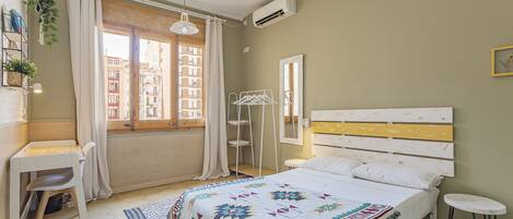 A bedroom with a bed, a desk, a chair, a hanging plant, and a window with curtains.