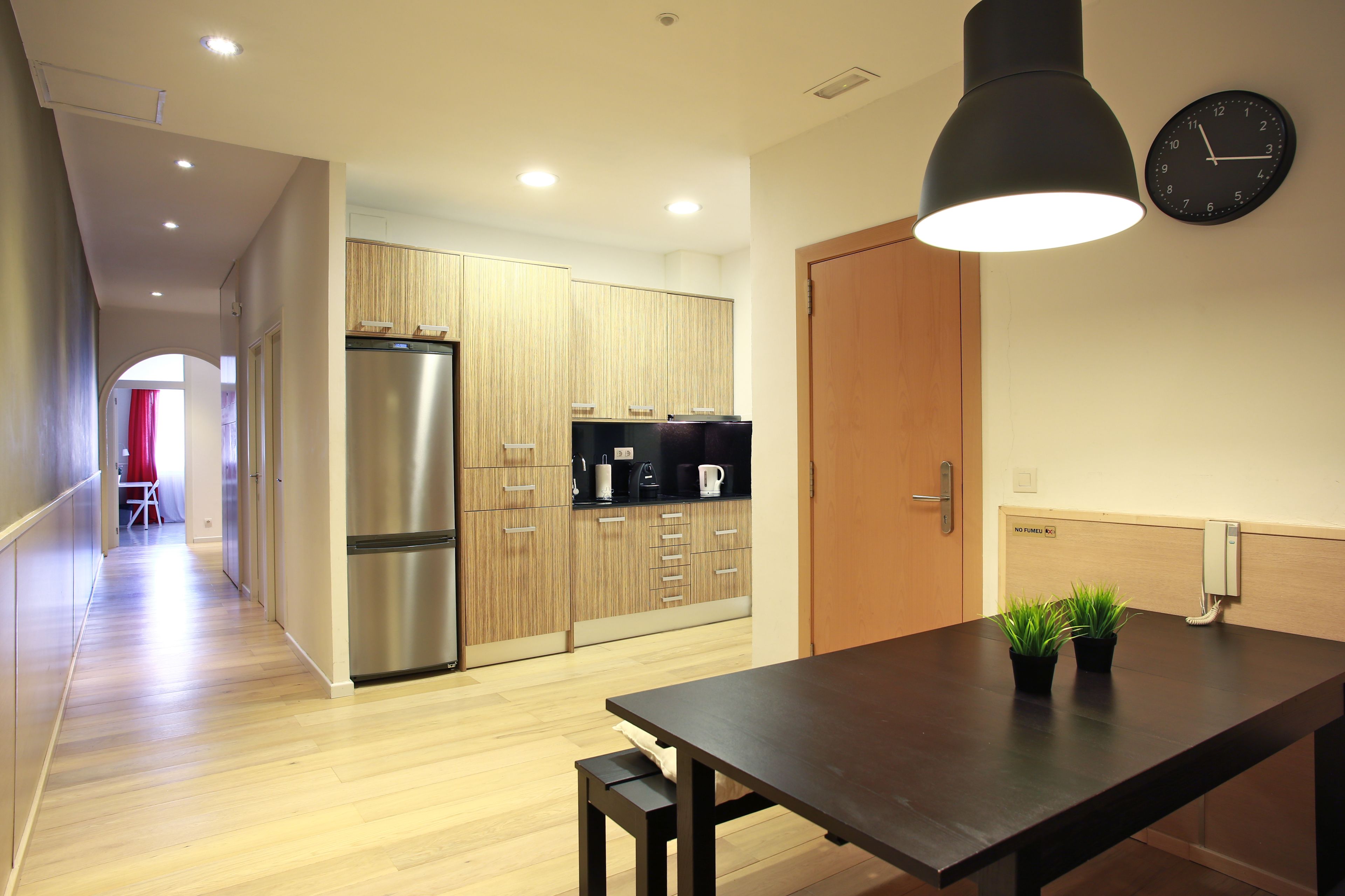 A modern kitchen with wooden cabinets, a stainless steel refrigerator, a black countertop, and a dining table with two potted plants.