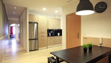 A modern kitchen with wooden cabinets, a stainless steel refrigerator, a black countertop, and a dining table with two potted plants.