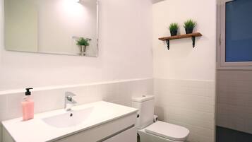 Een badkamer met een wit wastafelmeubel, toilet, spiegel en twee planten in potten op een plank.