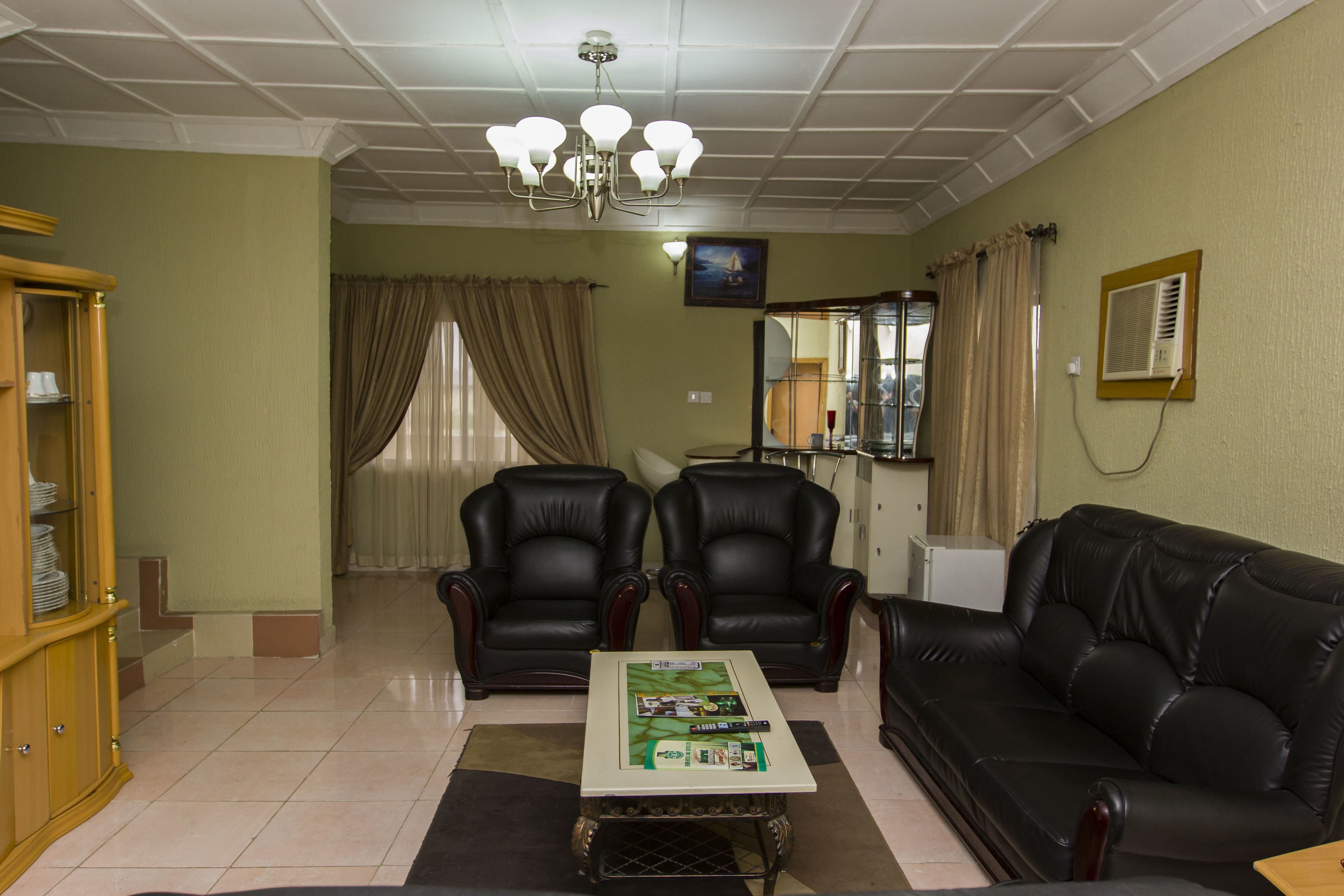 A living room with a black leather sofa, two leather armchairs, a wooden cabinet, a coffee table, and a ceiling light fixture.