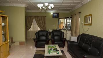 A living room with a black leather sofa, two leather armchairs, a wooden cabinet, a coffee table, and a ceiling light fixture.