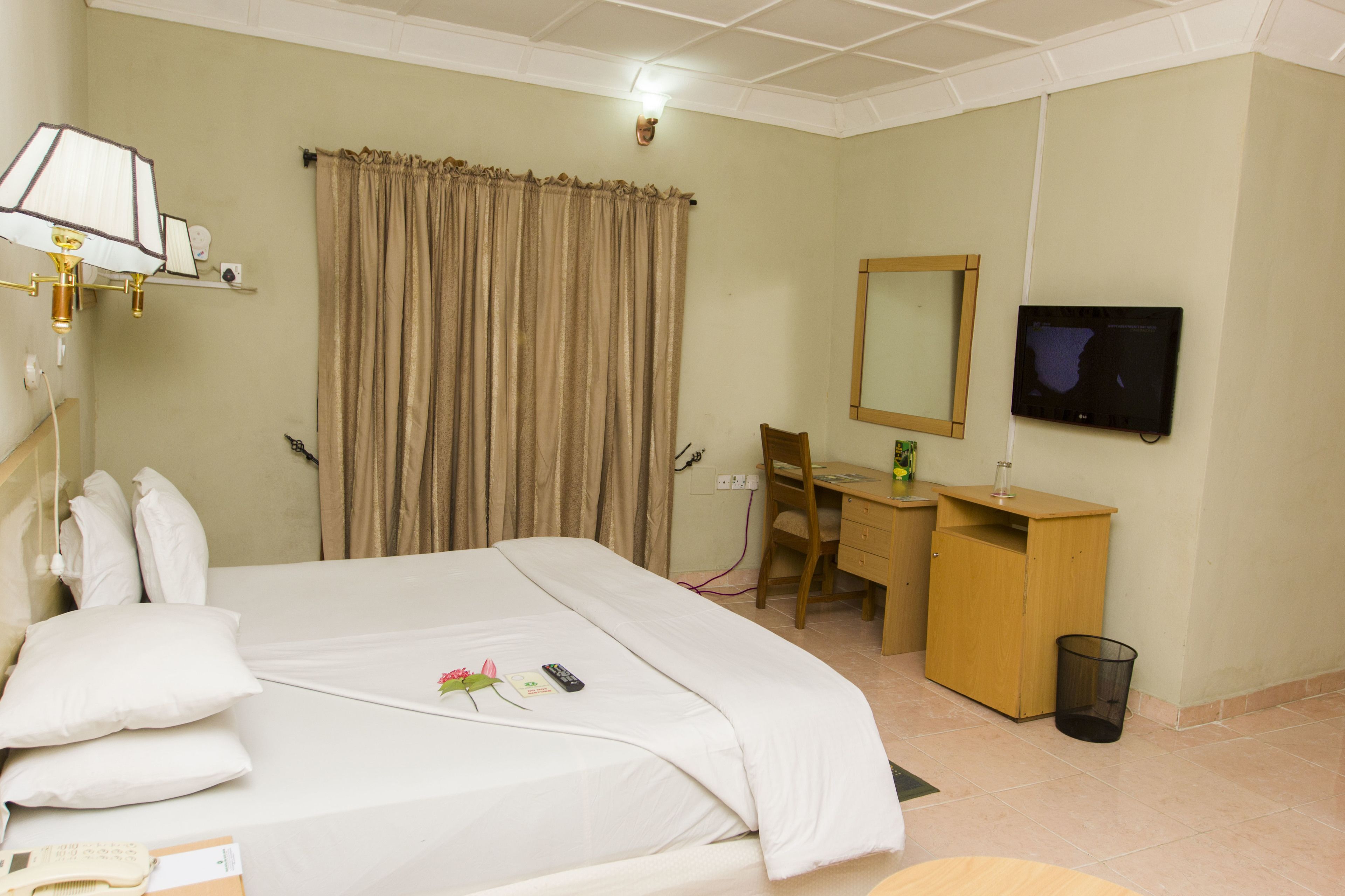A hotel room with a bed, a desk, a chair, a TV, and a trash bin.