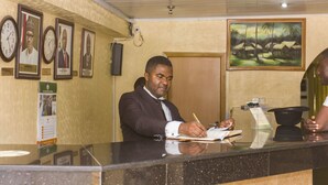 A reception desk with framed photographs on the wall, a clock, and a painting. - EEMJM Hotels and Suites Limited (Uyo)