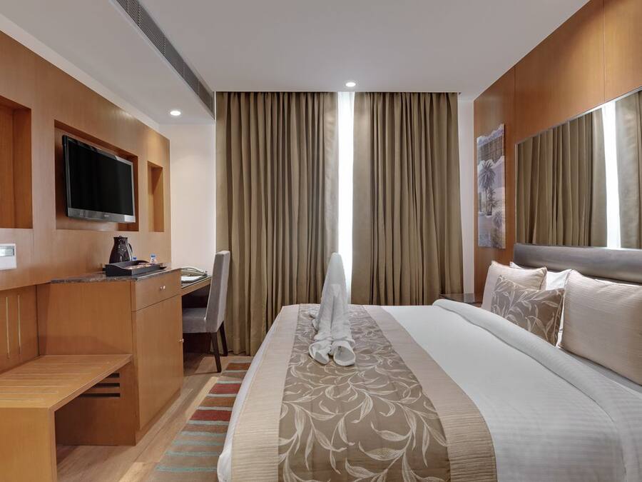 Habitación de hotel con cama, escritorio, silla, televisor y ventana con cortinas.