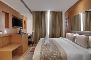 A hotel room with a bed, a desk, a chair, a television, and a window with curtains. - Beacon Hotel Nirman Vihar New Delhi (New Delhi)
