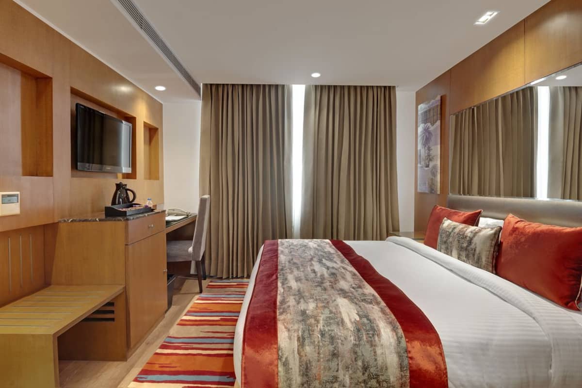Una camera d'albergo con un letto, una scrivania, una sedia, una televisione e tende.