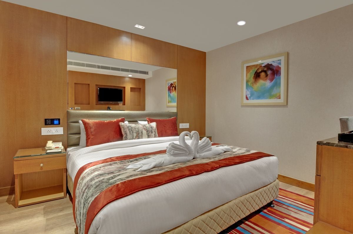 A hotel room with a large bed, a bedside table with a phone, a mirror, and artwork on the wall.