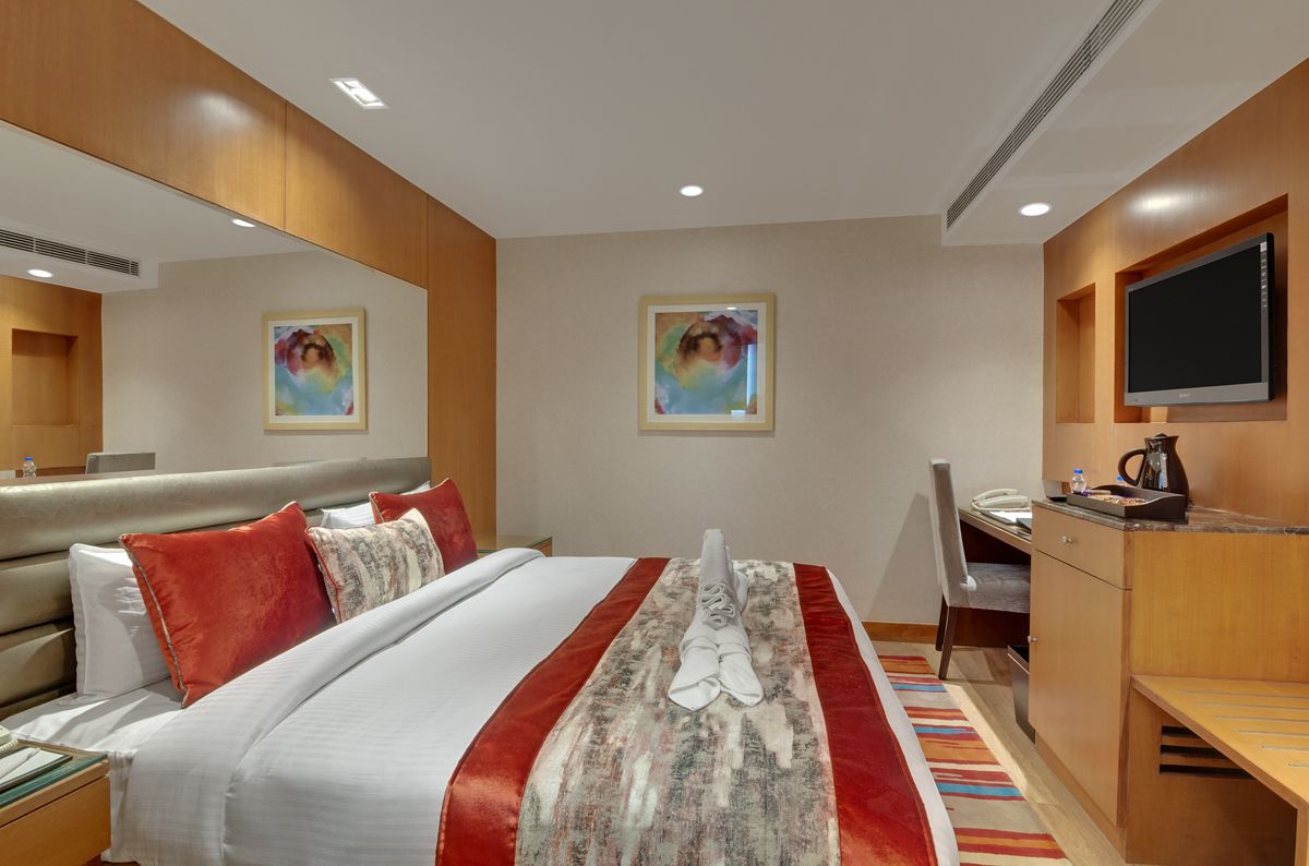 Habitación de hotel con cama, escritorio, silla, televisión y obras de arte en las paredes.