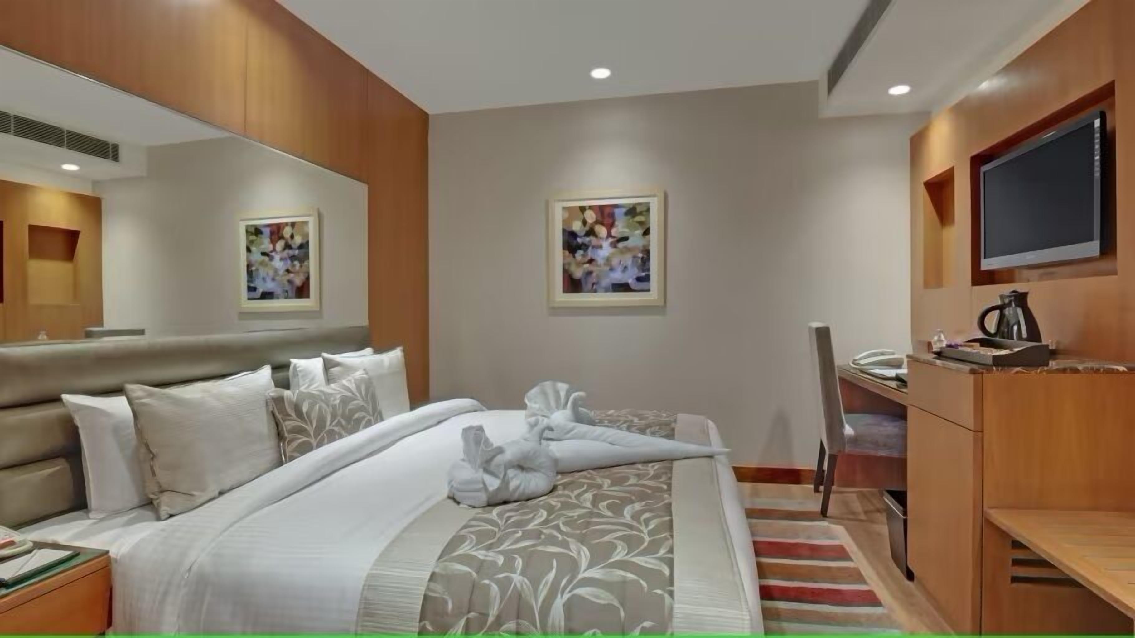 Habitación de hotel con cama, escritorio, silla, televisor y obras de arte en las paredes.