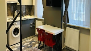 A compact kitchen with a washing machine, a dining table with red chairs, a TV, and a window with curtains. - Inci Konaklama (Isparta)