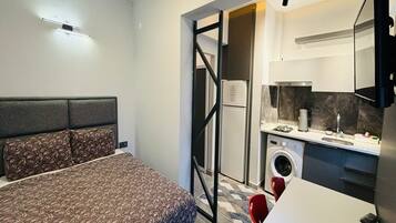 A compact bedroom with a bed, a small kitchenette, and a washing machine.
