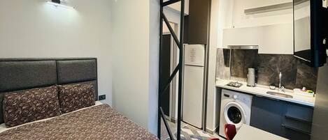 Un dormitorio compacto con cama, una kitchenette pequeña y una lavadora.