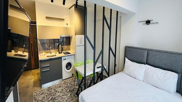 A modern hotel room with a bed, a desk, a washing machine, and a kitchenette. - Inci Konaklama (Isparta)