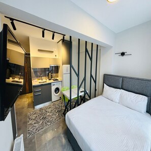 Una habitación de hotel moderna con cama, escritorio, lavadora y kitchenette.