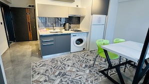 A compact kitchen with a washing machine, a coffee maker, and a dining area with a table and chairs. - Inci Konaklama (Isparta)
