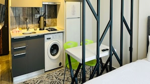 A compact hotel room with a kitchenette, a washing machine, a dining table with chairs, and a bed. - Inci Konaklama (Isparta)