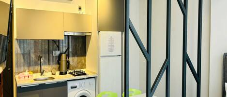 Una habitación de hotel compacta con kitchenette, lavadora, mesa de comedor con sillas y una cama.