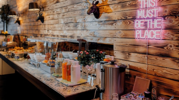 A buffet setup with wooden wall decor, a neon sign, and various food and drink items. - Jaeger's Munich - Hostel (Munich)