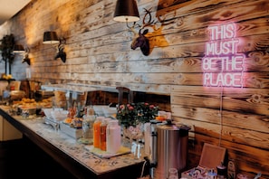 A buffet setup with wooden wall decor, a neon sign, and various food and drink items. - Jaeger's Munich - Hostel (Munich)