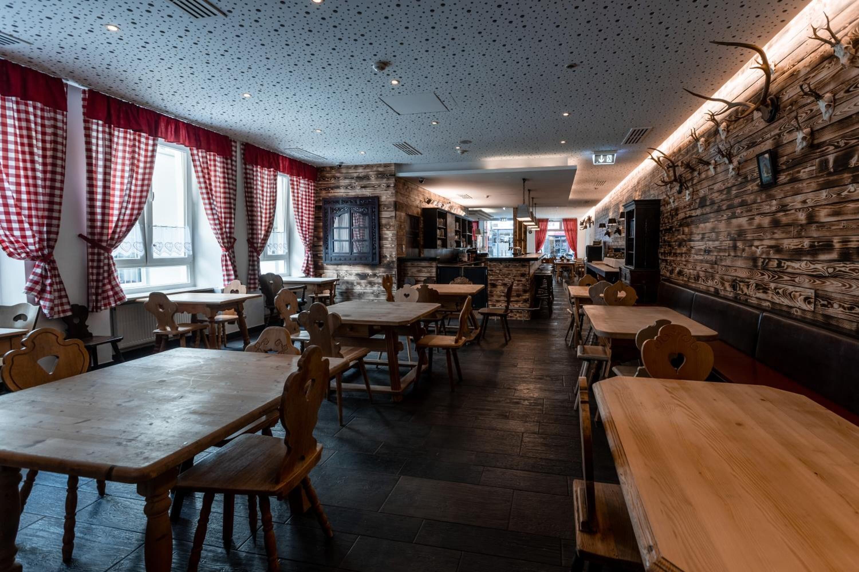 Un restaurant avec des tables et des chaises en bois, des rideaux à carreaux rouges et blancs et un plafond à motifs.