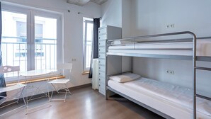 A dormitory room with bunk beds, a desk, chairs, and a window with a view. - Jaeger's Munich - Hostel (Munich)