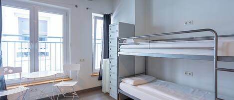 A dormitory room with bunk beds, a desk, chairs, and a window with a view.