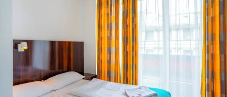 A hotel room with a wooden headboard, two beds, a blue blanket, and curtains with a checkered pattern.