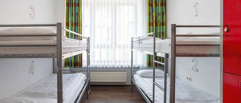 A dormitory room with bunk beds numbered 1 to 4, a radiator, and a window with curtains.