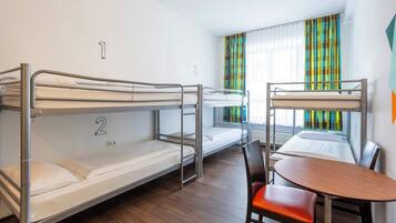 Ein Schlafsaalzimmer mit Etagenbetten, Holzboden, einem kleinen Tisch und bunten Vorhängen.