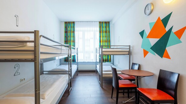 A dormitory room with bunk beds, a small table, chairs, and a clock on the wall. - Jaeger's Munich - Hostel (Munich)
