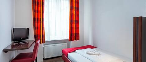 A hotel room with a bed, a desk with a television, a chair, and a window with curtains.