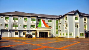 A large building with multiple windows and air conditioning units, a central entrance with a flag, and a parking area with orange lines. - NEW POINT HOTEL AND SUITES (Uyo)