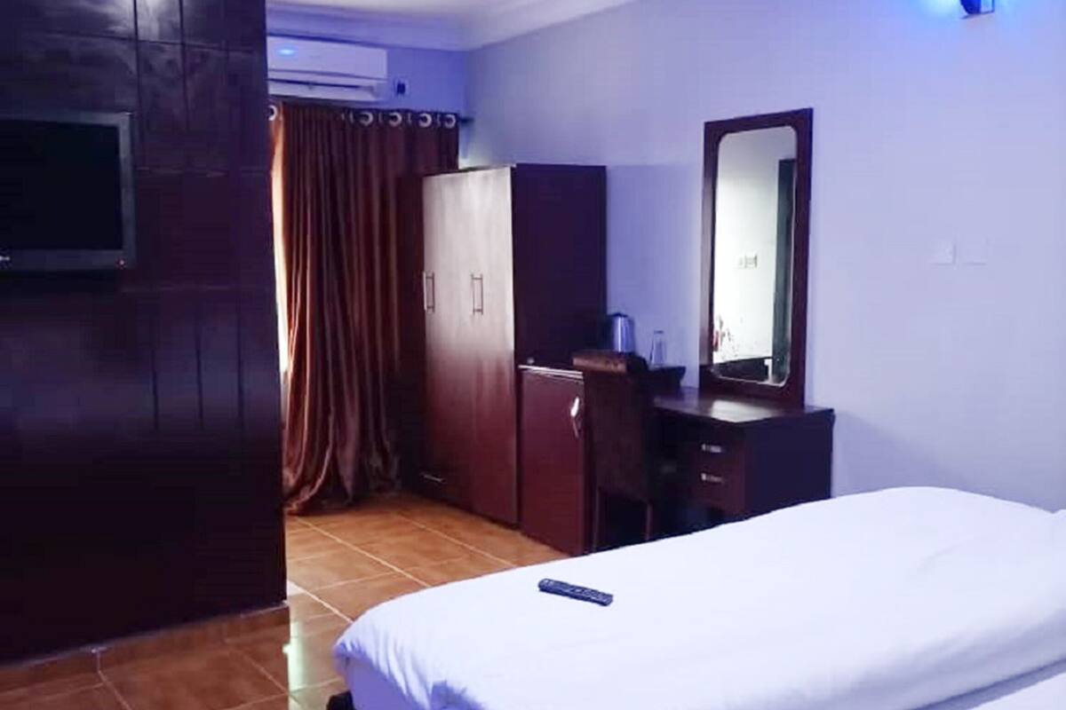 A hotel room with a bed, a desk, a mirror, a TV, and a wardrobe.
